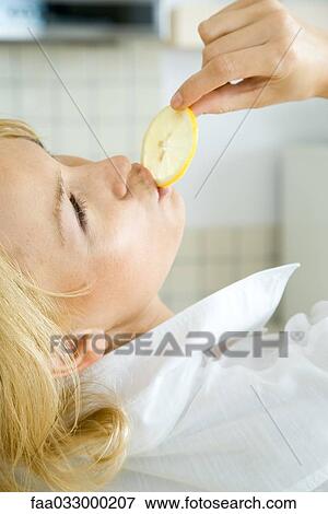 Stock Photo - Woman eating lemon slice, head back, cropped view. Fotosearch