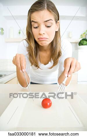 Woman frowning down at single cherry tomato on plate, holding fork and knife View Large Photo Image Stock Image - Woman frowning down at single cherry tomato on plate, holding fork and knife. Fotosearch