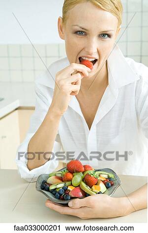Woman holding bowl of fruit salad, eating strawberry, looking at camera View Large Photo Image Stock Image - Woman holding bowl of fruit salad, eating strawberry, looking at camera. Fotosearch