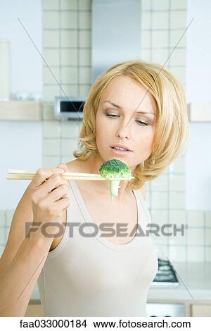 Woman holding broccoli with chopsticks, looking down View Large Photo Image Picture - Woman holding broccoli with chopsticks, looking down. Fotosearch