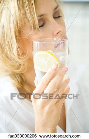 Woman holding glass of mineral water against cheek, eyes closed View Large Photo Image Stock Photograph - Woman holding glass of mineral water against cheek, eyes closed. Fotosearch