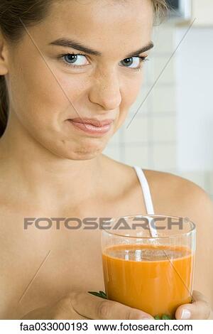 Stock Image - Woman holding glass of vegetable juice, frowning at camera. Fotosearch
