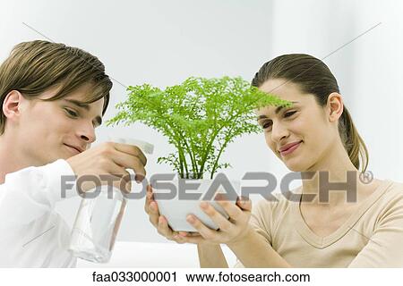 Stock Image - Woman holding potted plant, man using spray bottle. Fotosearch