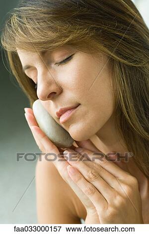Stock Photo - Woman holding smooth stone against face. Fotosearch