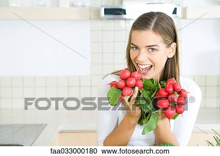 Stock Image - Woman holding up bunches of fresh radishes, smiling at camera. Fotosearch
