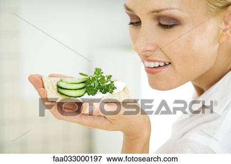 Woman holding up cracker with cucumber slices, smiling View Large Photo Image Stock Photo - Woman holding up cracker with cucumber slices, smiling. Fotosearch
