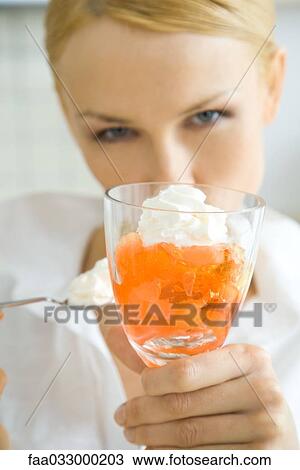 Stock Image - Woman holding up fruit dessert, looking at camera. Fotosearch