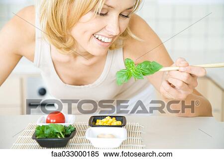 Woman leaning over, holding fresh basil with chopsticks, smiling View Large Photo Image Stock Photography - Woman leaning over, holding fresh basil with chopsticks, smiling. Fotosearch