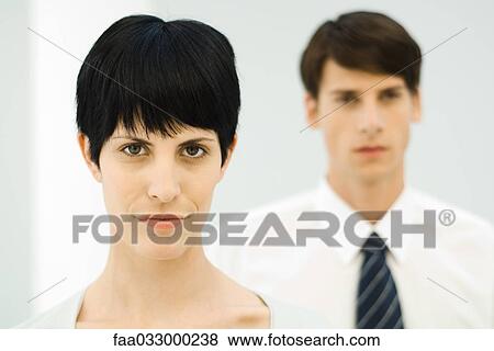 Stock Photo - Woman looking at camera, close-up, male colleague in background. Fotosearch