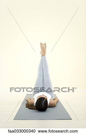 Stock Image - Woman lying on back with legs raised in the air. Fotosearch