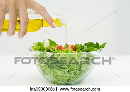 Stock Image - Woman pouring olive oil on salad, cropped view of hand. Fotosearch