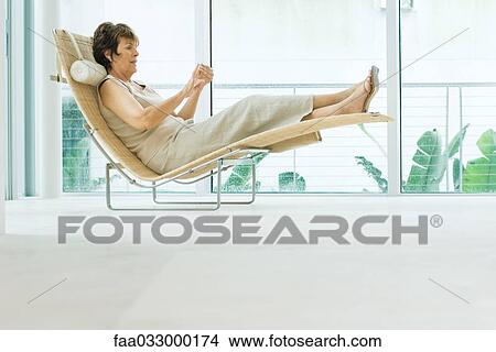 Woman reclining on lounge chair, side view View Large Photo Image Picture - Woman reclining on lounge chair, side view. Fotosearch