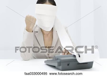 Stock Photography - Woman sitting at desk, tape from an adding machine wrapped around her head, clenching fist. Fotosearch