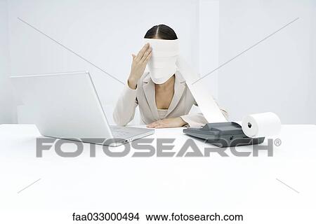 Picture - Woman sitting behind adding machine, roll paper wrapped around her head. Fotosearch