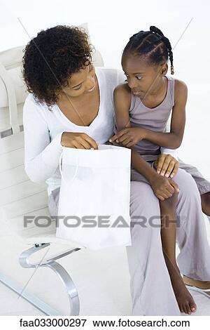 Stock Photo - Woman sitting in chair, holding gift bag, daughter sitting in her lap, both looking down. Fotosearch