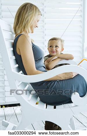 Picture - Woman sitting in chair next to son, both smiling at each other. Fotosearch