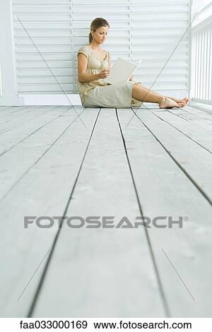 Stock Photo - Woman sitting on porch reading book, low angle view. Fotosearch