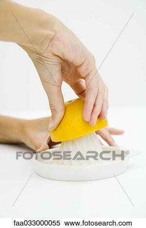 Stock Photography - Woman squeezing orange with citrus press, cropped view of hands. Fotosearch