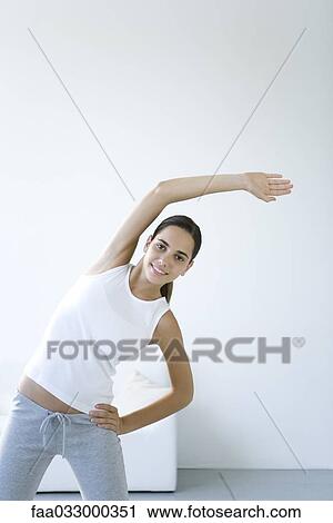 Stock Image - Woman stretching, one arm raised, smiling at camera. Fotosearch