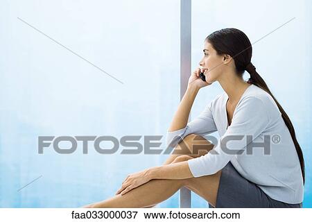 Stock Photo - Woman talking on cell phone, looking out window, sitting. Fotosearch
