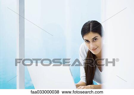 Stock Photo - Woman using laptop, smiling at camera, cropped. Fotosearch