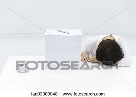 Stock Image - Woman with head down on desk, next to tall stack of papers. Fotosearch