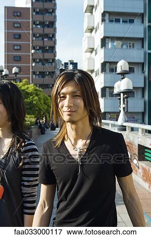 Stock Photo - Young couple walking in urban setting, man smiling at camera, cropped. Fotosearch