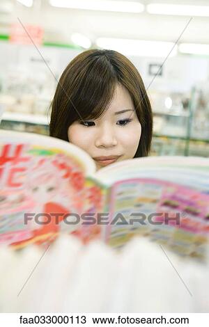 Stock Image - Young Japanese woman reading comic book, selective focus. Fotosearch