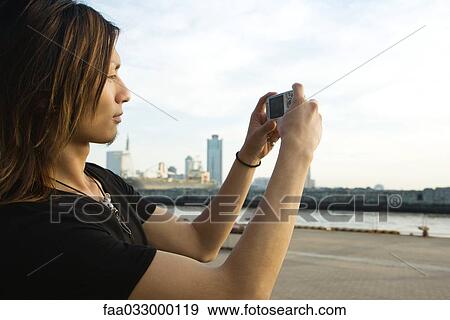 Stock Photo - Young man photographing waterfront with digital camera, side view. Fotosearch
