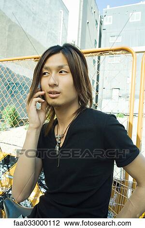 Stock Image - Young man using cell phone, looking away. Fotosearch