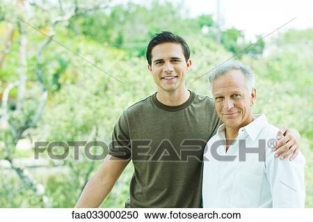 Stock Image - Young man with arm around his father's shoulder, both smiling at camera, portrait. Fotosearch