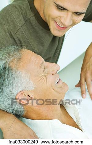 Stock Photo - Young man with arm around his father's shoulder, smiling at each other. Fotosearch