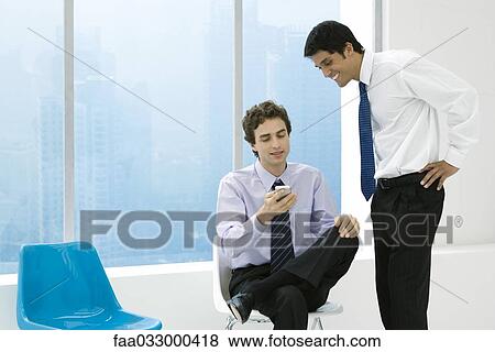 Stock Photo - Young professional showing colleague his cell phone, both smiling. Fotosearch