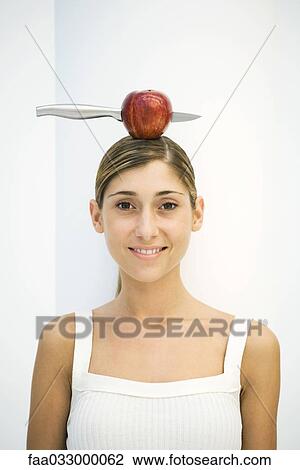 Young woman balancing apple with a knife stuck in it on head, portrait View Large Photo Image Stock Image - Young woman balancing apple with a knife stuck in it on head, portrait. Fotosearch
