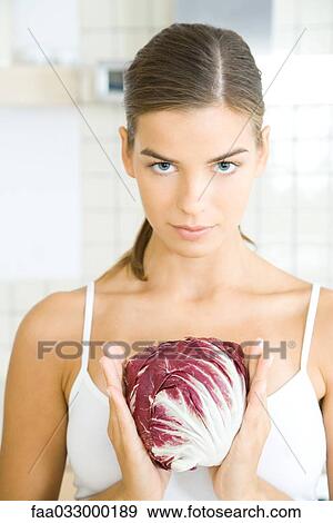 Stock Photo - Young woman holding head of chicory, looking at camera. Fotosearch