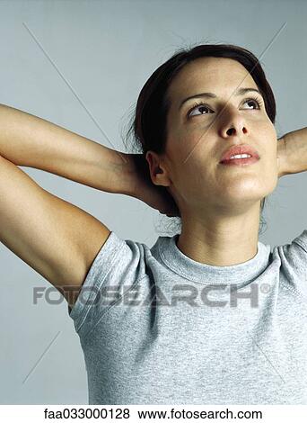 Stock Photo - Young woman with hands behind head, looking up, portrait. Fotosearch