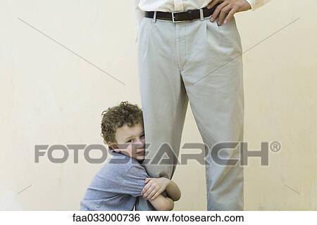 Boy clinging to his father's leg, looking at camera, cropped view View Large Photo Image Stock Photograph - Boy clinging to his father's leg, looking at camera, cropped view. Fotosearch