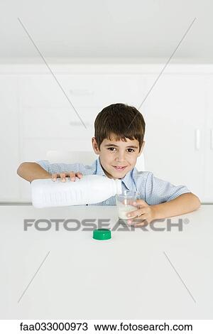 Stock Image - Boy pouring milk into empty glass, smiling at camera. Fotosearch
