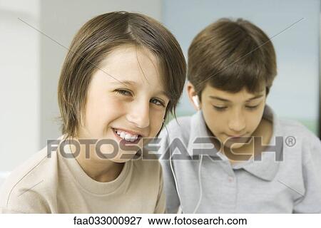 Boys sharing earphones, one smiling at camera, other looking down View Large Photo Image Stock Photo - Boys sharing earphones, one smiling at camera, other looking down. Fotosearch