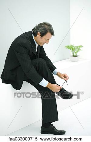 Businessman sitting on ledge, tying shoe View Large Photo Image Stock Photography - Businessman sitting on ledge, tying shoe. Fotosearch