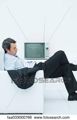 Stock Photograph - Businessman taking a nap in armchair, slouching with legs crossed, side view. Fotosearch