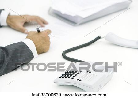 Businessman writing on document, phone off the hook nearby, cropped view View Large Photo Image Stock Photo - Businessman writing on document, phone off the hook nearby, cropped view. Fotosearch