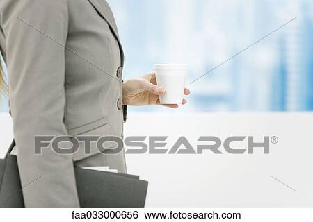 Stock Photograph - Businesswoman holding disposable coffee cup and briefcase, cropped side view. Fotosearch