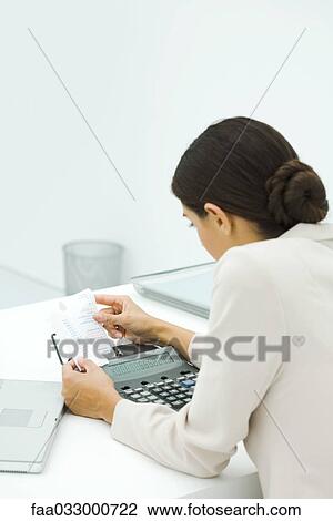 Stock Image - Businesswoman using adding machine, holding receipt, rear view. Fotosearch