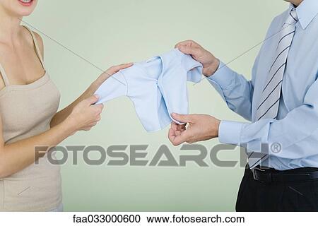 Stock Image - Couple holding up baby clothing together, cropped view. Fotosearch