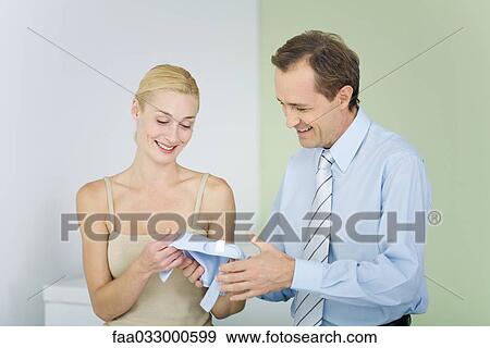 Stock Photo - Couple looking at baby clothing together, both smiling. Fotosearch