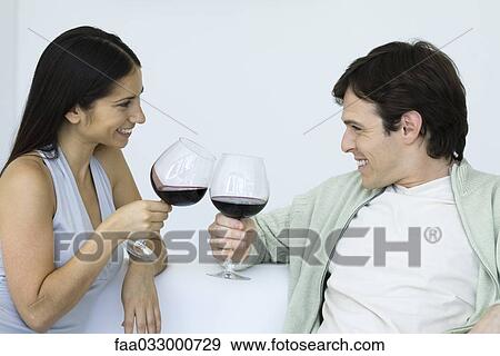 Couple sitting on couch, clinking wine glasses, smiling at each other View Large Photo Image Stock Photo - Couple sitting on couch, clinking wine glasses, smiling at each other. Fotosearch