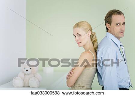 Couple standing back to back in nursery, looking over shoulders at camera, woman's arms folded View Large Photo Image Stock Photo - Couple standing back to back in nursery, looking over shoulders at camera, woman's arms folded. Fotosearch