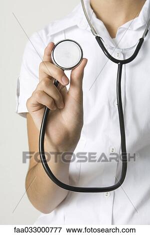 Stock Photo - Doctor holding stethoscope and showing it to camera, cropped view. Fotosearch