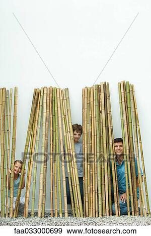Stock Photo - Father and two children peeking through bamboo at camera, all smiling. Fotosearch